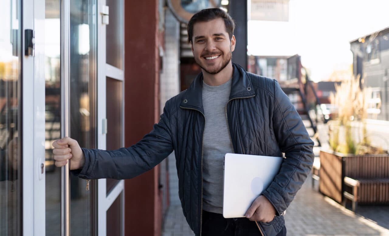 a male IT specialist with a laptop in his hands enters the office building with a wide smile on his face